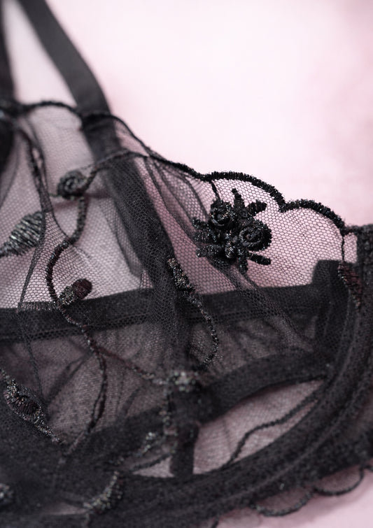 Black lace lingerie with floral embroidery on a light pink background