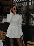 Заредете изображението в програмата за преглед на галерия, Woman in a white blazer dress with belt standing in an indoor setting with tables and chairs.