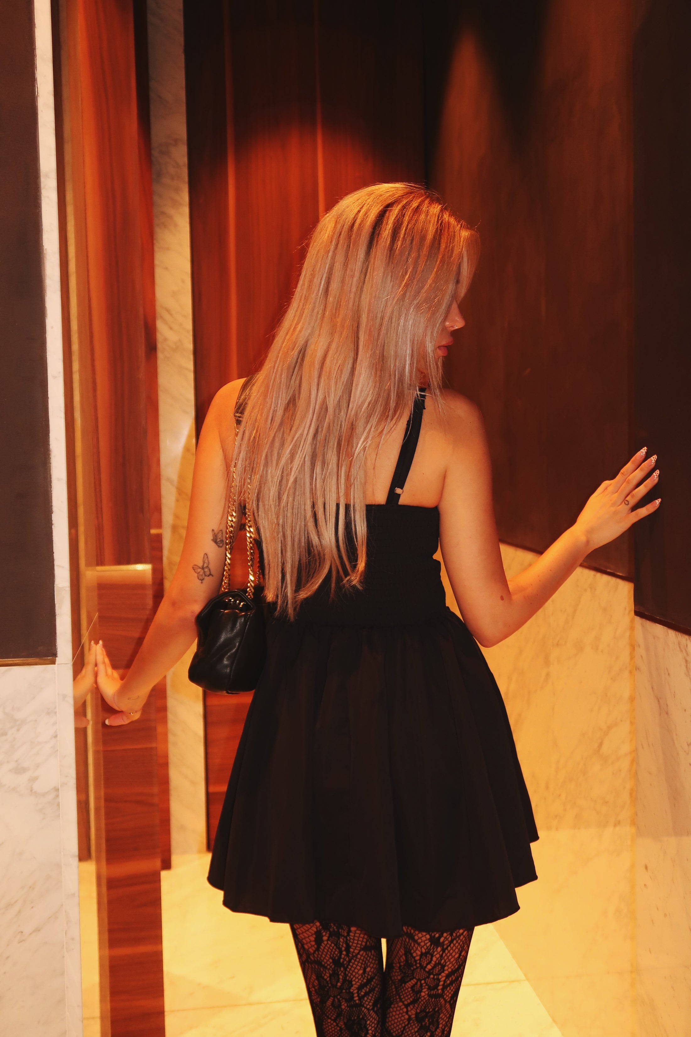 Woman in a black dress standing in front of a mirror.