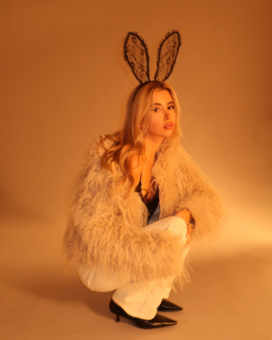 Person wearing a fluffy white coat and bunny ears on a brown background