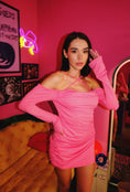Load image into Gallery viewer, A person wearing a hot pink off-the-shoulder mini dress with ruched detailing and a criss-cross neckline.