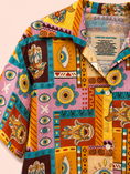 Заредете изображението в програмата за преглед на галерия, A close-up of a short-sleeve button-up shirt with a vibrant, multicolor patchwork print featuring tribal eye motifs, hamsa hands, and geometric patterns in yellow, orange, pink, teal, and brown. The inside collar shows a label that reads 'LIMITED EDITION'.