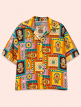 Заредете изображението в програмата за преглед на галерия, A short-sleeve button-up shirt with a vibrant, multicolor patchwork print featuring Hamsa hands, eyes, and geometric tribal patterns in yellow, orange, pink, teal, and brown, laid flat against a pale peach background.
