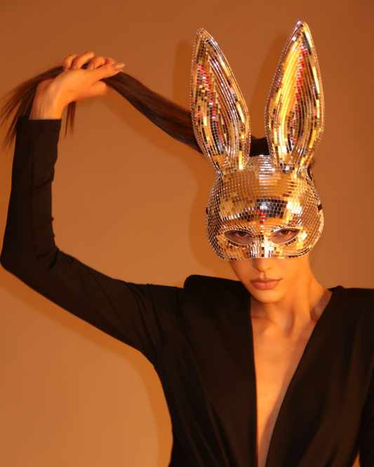 Person wearing a silver sequin bunny mask against a warm-toned background