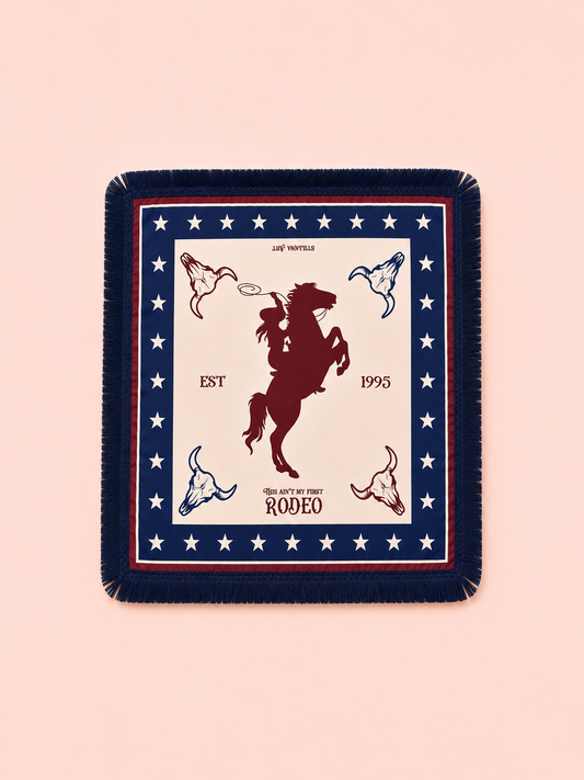 A square fringed throw scarf featuring a western rodeo theme, displayed flat against a solid pale pink background. The blanket has a navy blue border with white stars, a red inner stripe, and a cream center panel showing a dark red rearing horse silhouette, cowboy boots, and text reading 'EST 1995' and 'RODEO'.