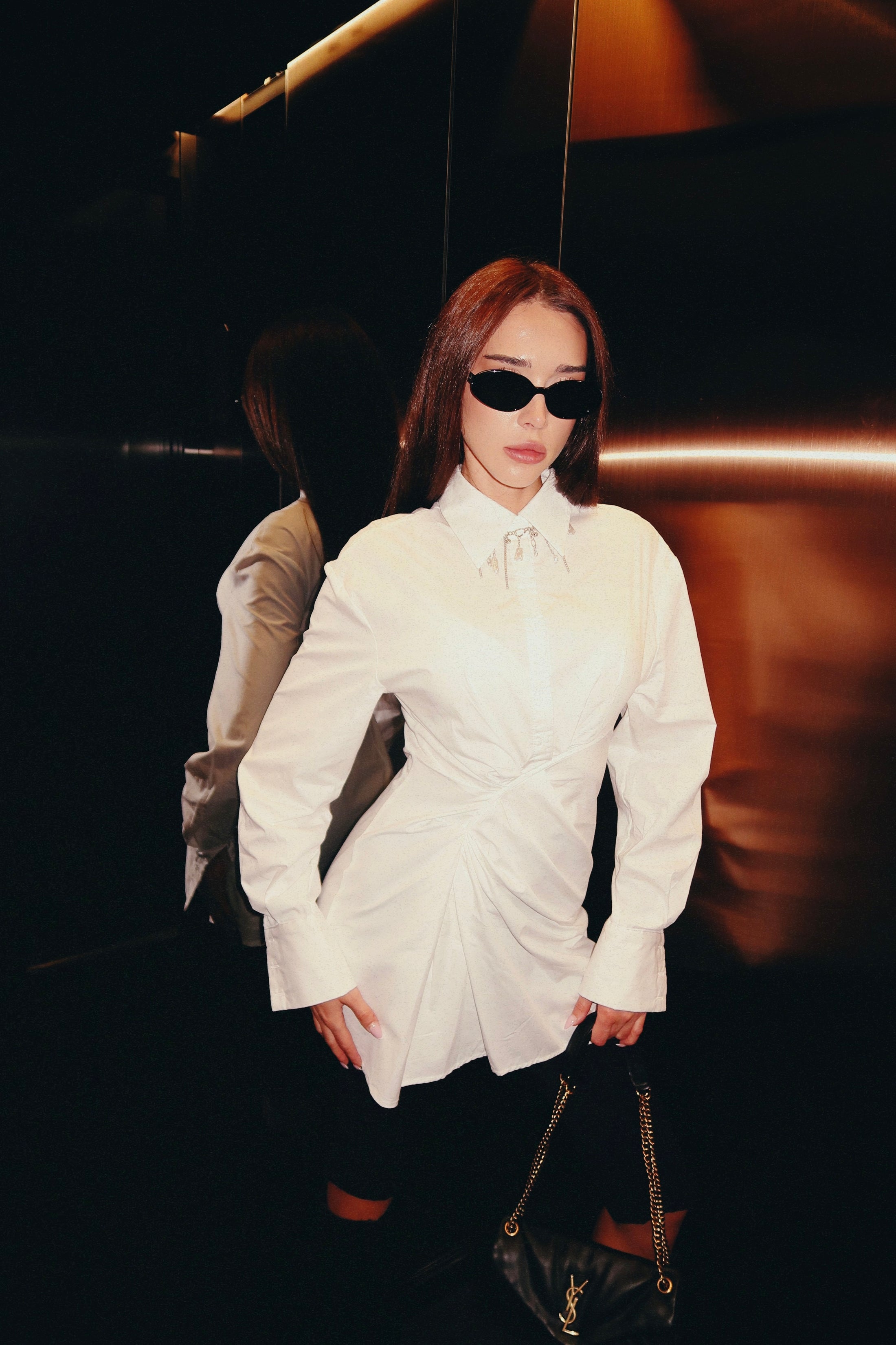 Person wearing a white shirt dress with ruffled details, holding a black handbag.