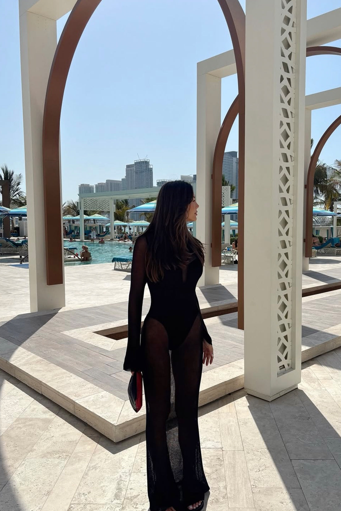 Woman in a black outfit standing in front of a pool with a cityscape in the background
