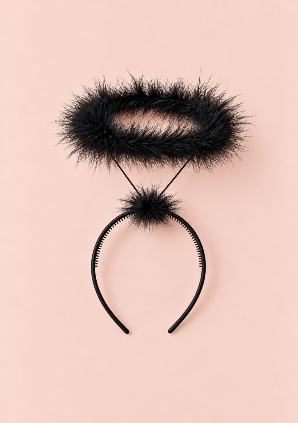A black furry headband with a matching fuzzy pom-pom and thin black elastic cords, laid flat on a solid pale pink background.