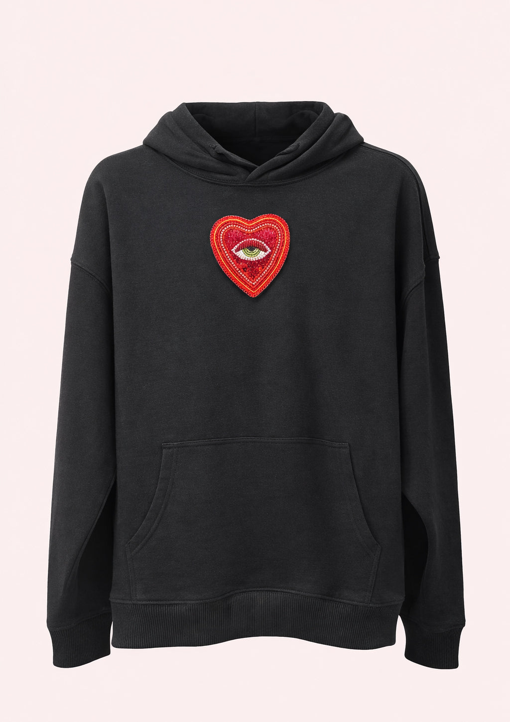 Black hoodie with a red heart patch featuring an eye on a light pink background