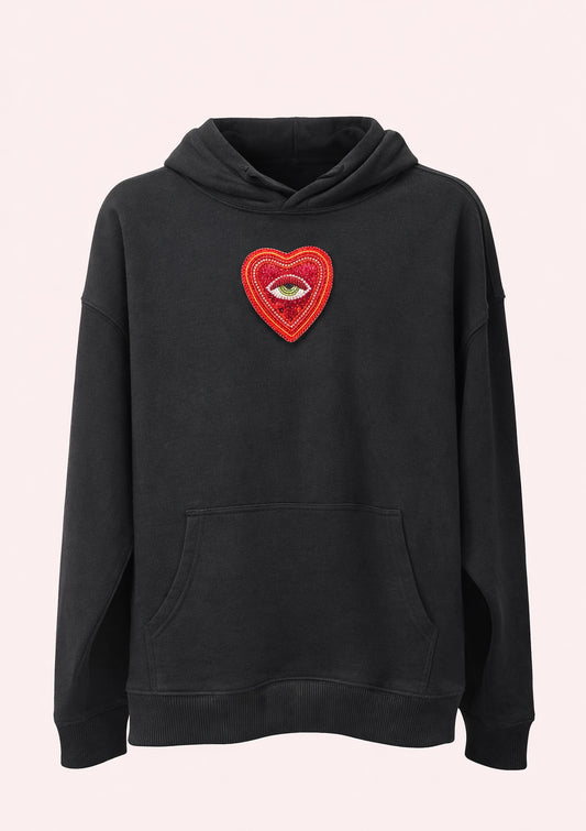 Black hoodie with a red heart patch featuring an eye on a light pink background