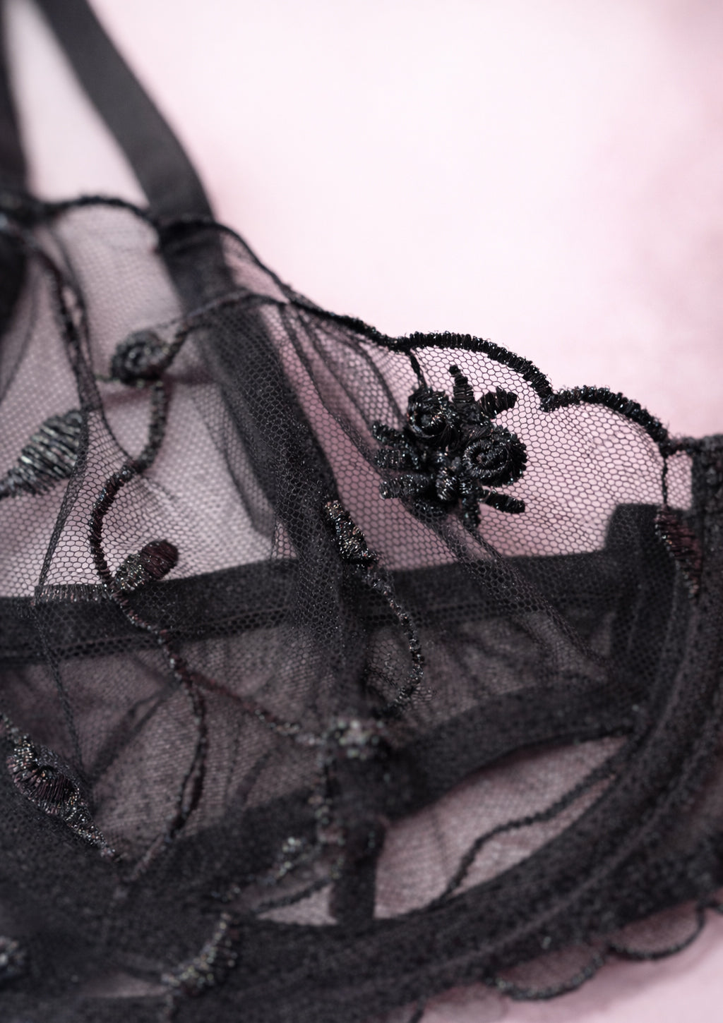 Black lace lingerie with floral embroidery on a light pink background