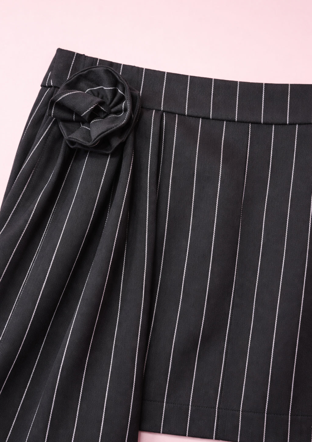 Black pinstripe skirt with a flower detail on a pink background