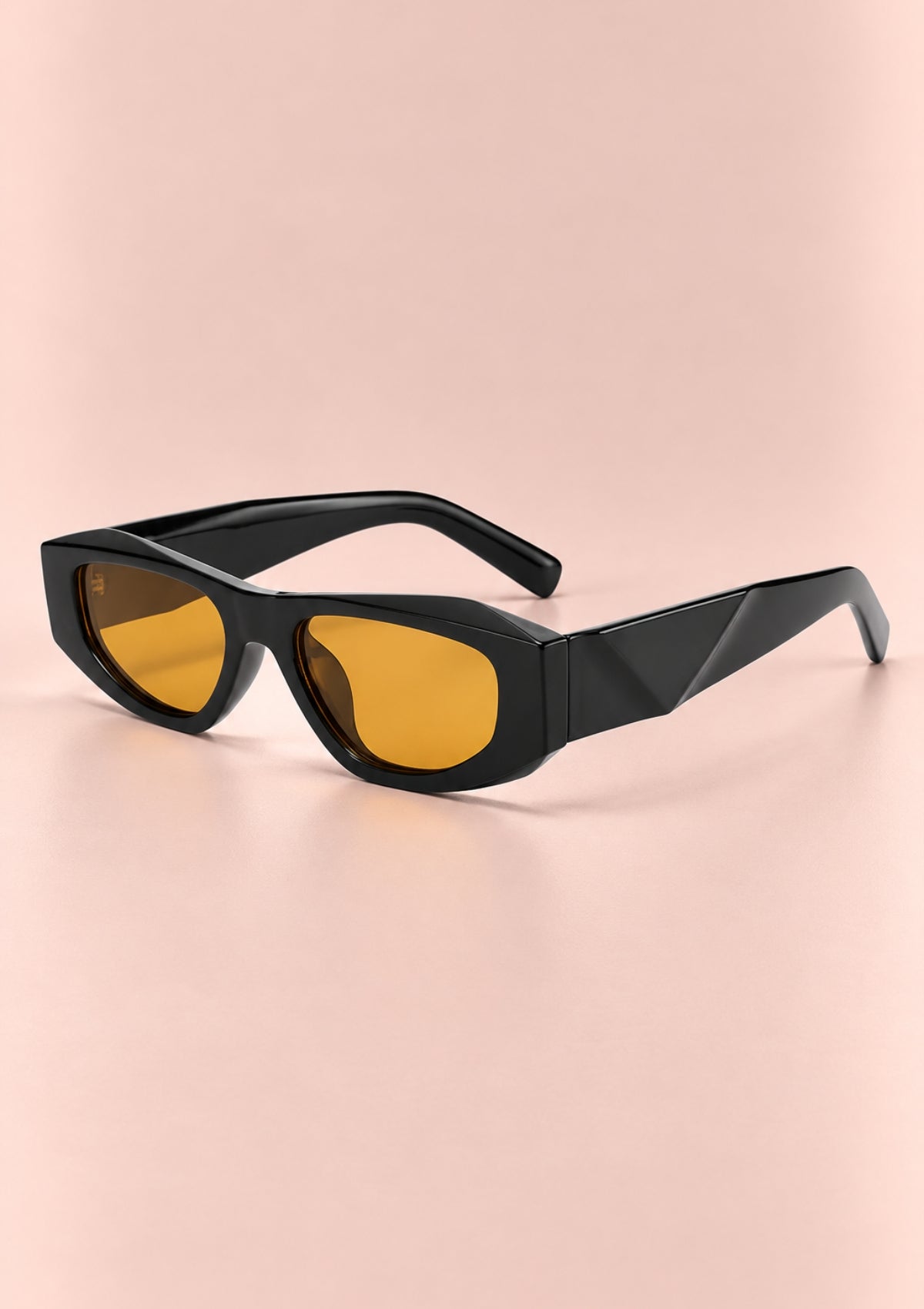 Black geometric sunglasses with yellow-orange tinted lenses, displayed on a soft pink background.