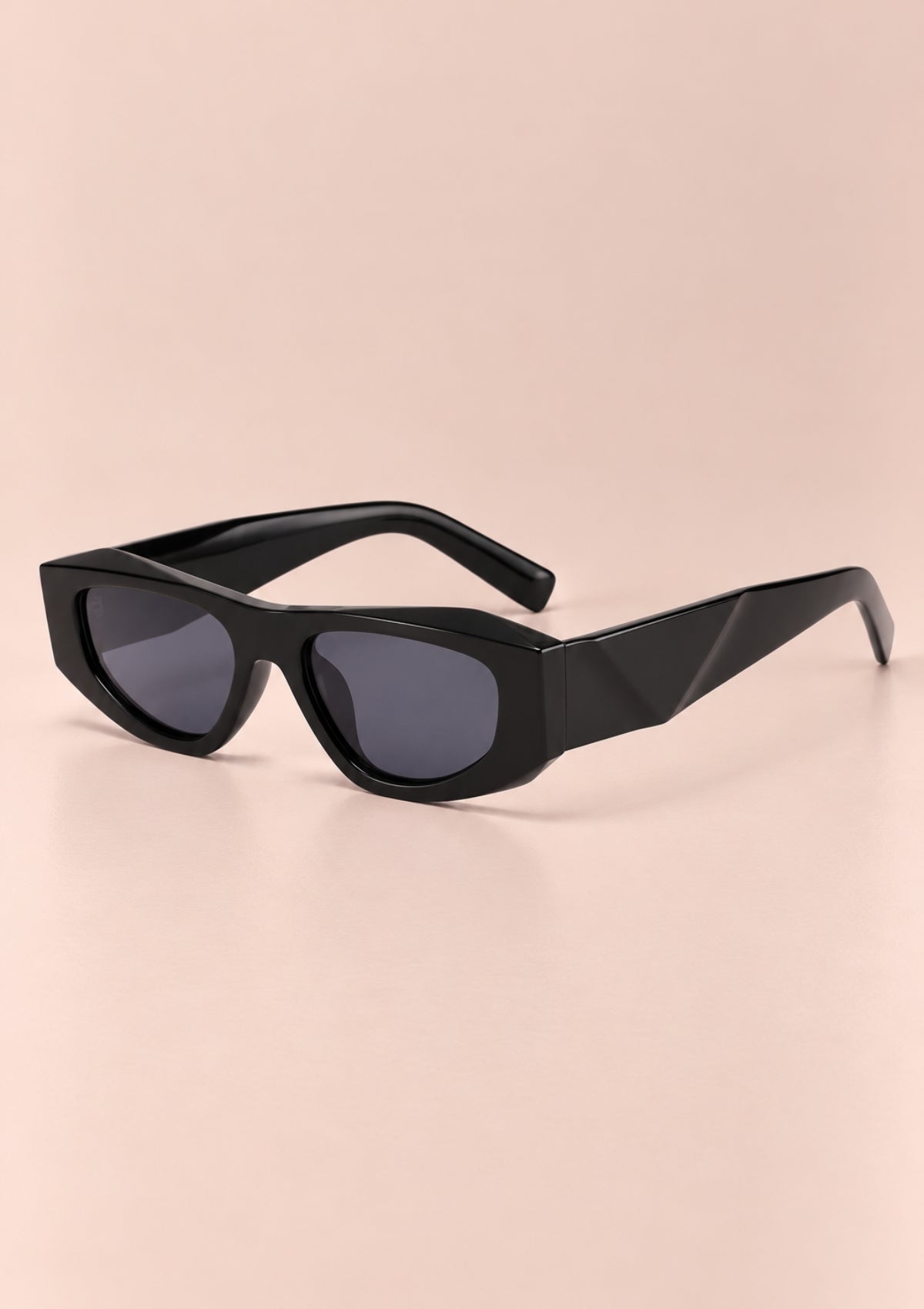 Black geometric sunglasses with dark tinted lenses, displayed on a soft beige-pink background.