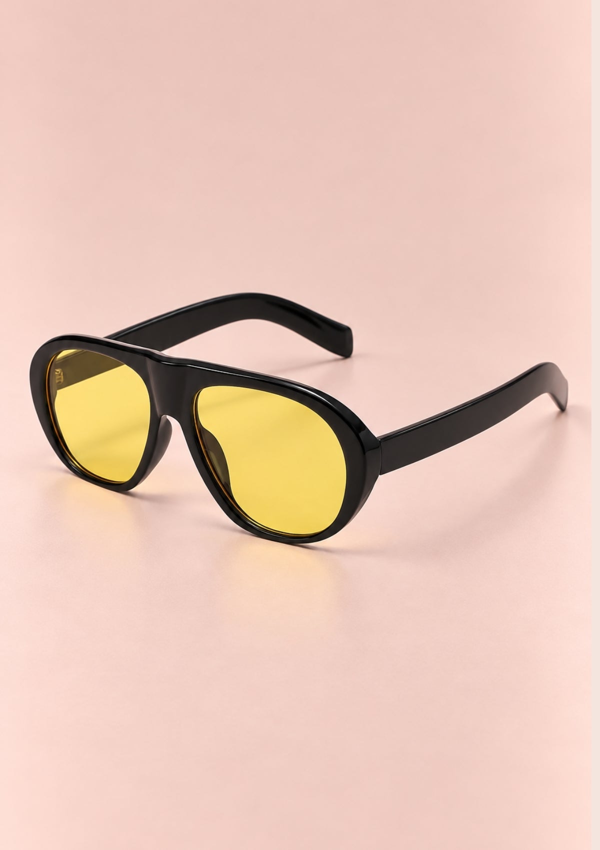 Black oversized sunglasses with yellow tinted lenses, displayed on a soft pink background.