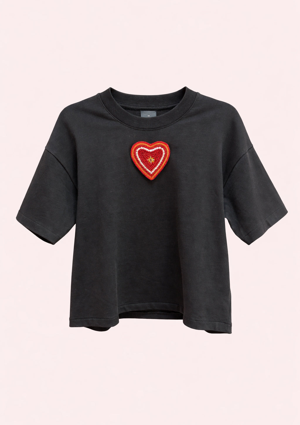 Black t-shirt with a red heart-shaped patch on a light pink background