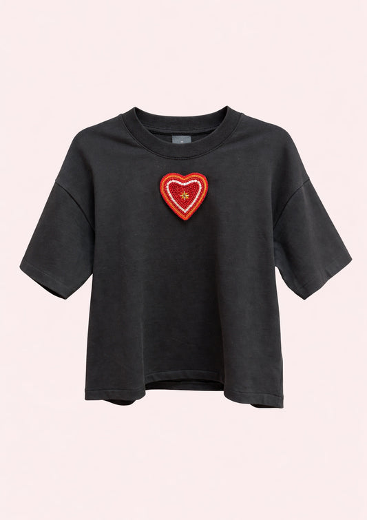 Black t-shirt with a red heart-shaped patch on a light pink background