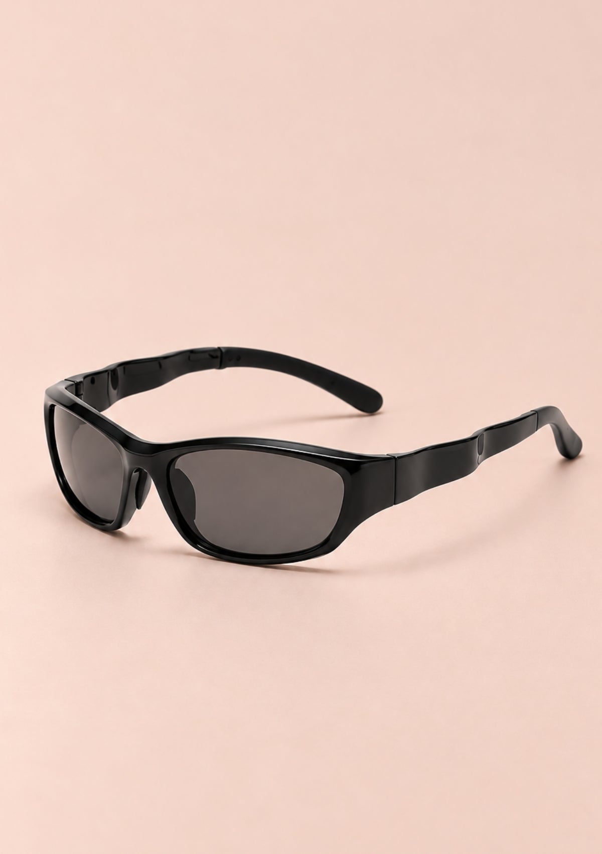 Black wrap-around sunglasses with dark tinted lenses, displayed on a solid pale pink background.