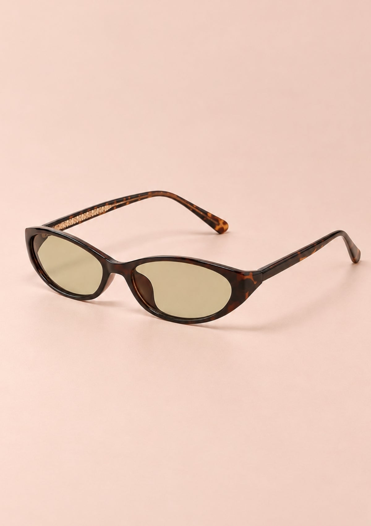 Oval cat-eye sunglasses with a dark brown tortoiseshell frame and light olive-green tinted lenses, displayed on a solid pale pink background.