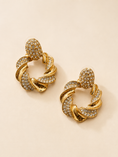 Load image into Gallery viewer, A pair of gold-toned twisted hoop earrings embellished with clear rhinestones, displayed on a light beige background.

