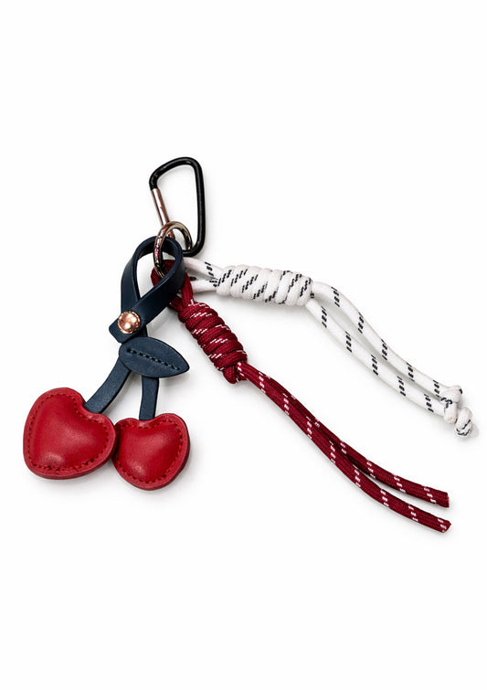 Add a playful pop of color to your everyday essentials with this Cherry Heart Charm. Featuring two glossy red heart-shaped cherries crafted from smooth faux leather, this charm is finished with contrasting cord details and a sturdy carabiner clasp for easy attachment. Perfect for keys, bags, or backpacks, it brings a fun, romantic touch while staying effortlessly stylish. A charming little accessory that makes a sweet statement wherever you clip it.