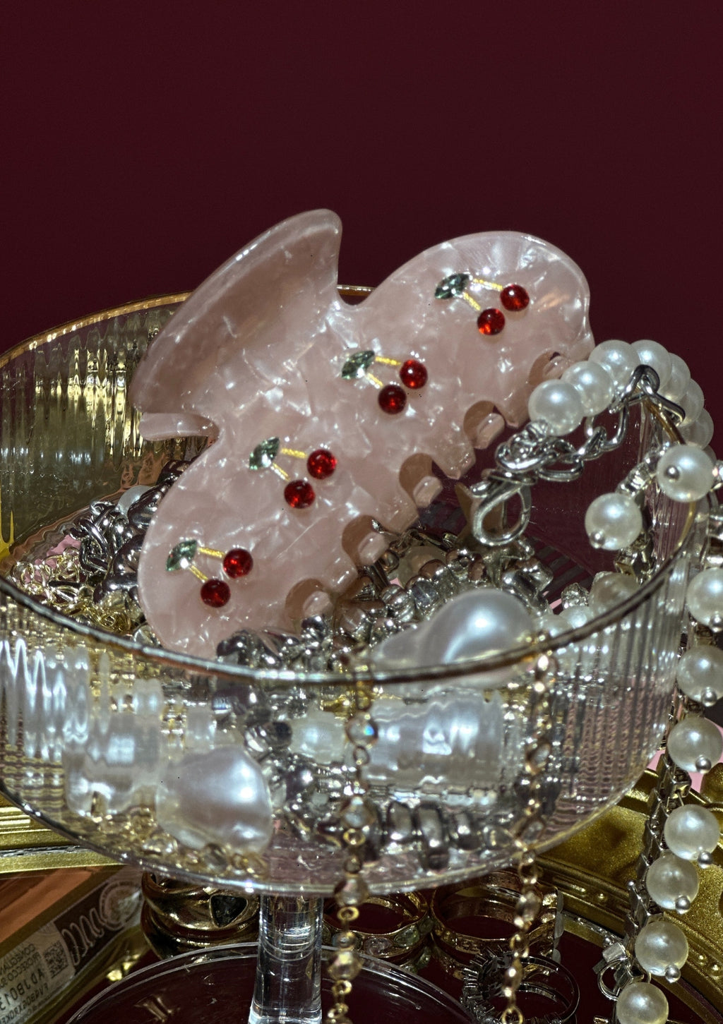 Decorative items including pink flowers with red berries and pearls in a glass bowl on a dark background