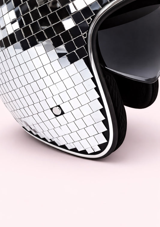 Close-up of a disco ball helmet with a black frame on a light pink background