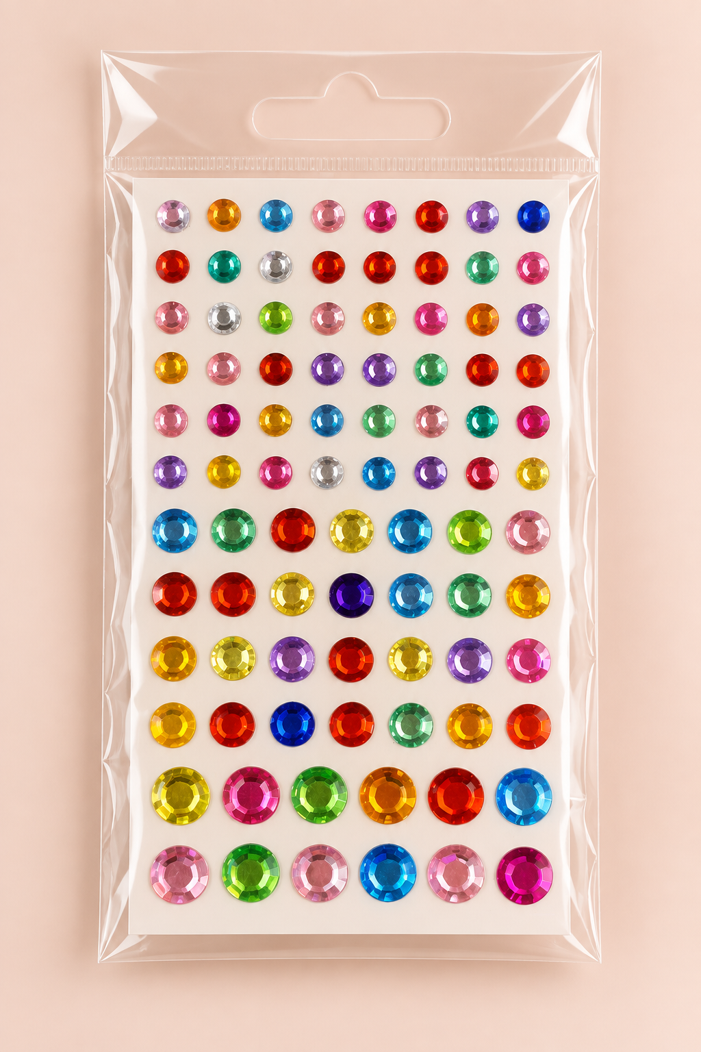 A package of colorful round rhinestone stickers on a white backing card, sealed in a clear plastic hanging bag, set against a solid pale pink background.