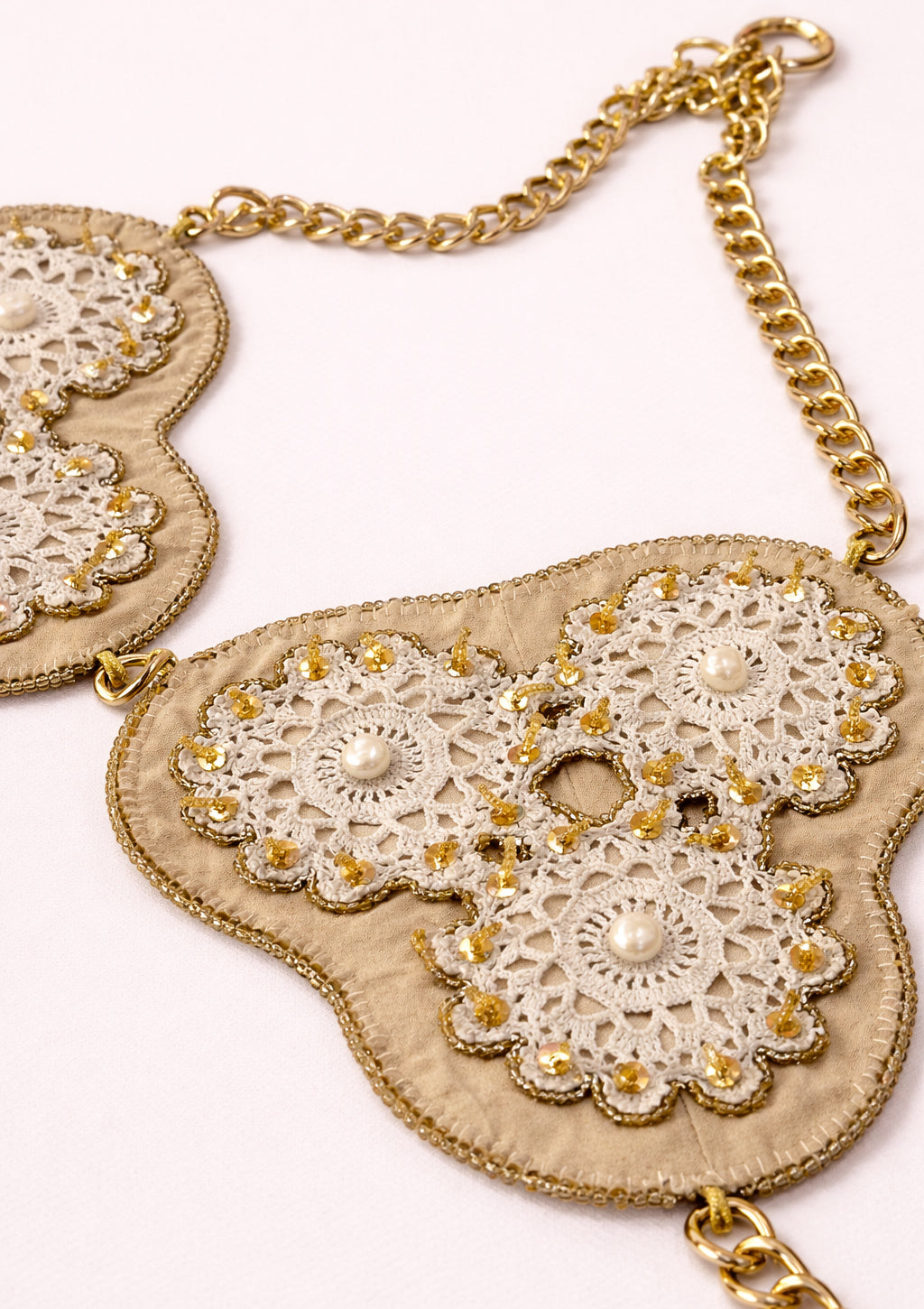 Decorative top with lace details and gold chain on a white background