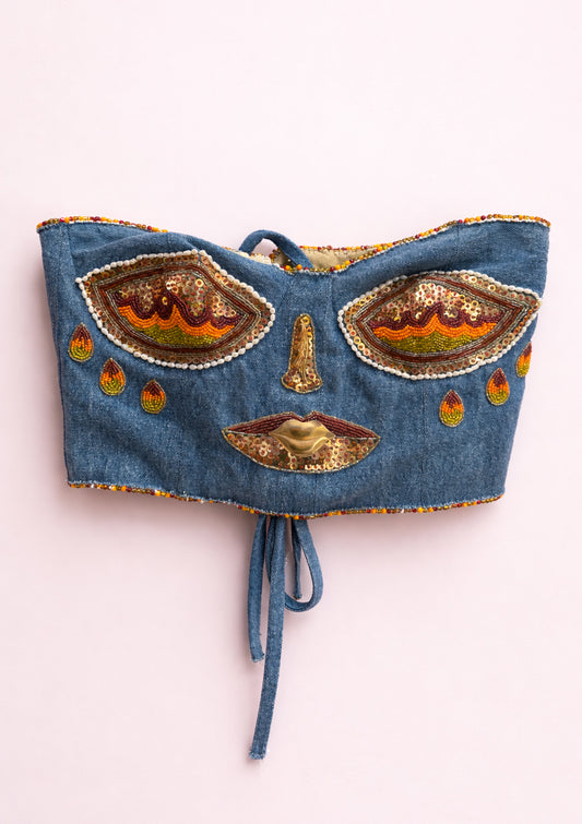 Denim crop top with decorative eye patterns on a white background