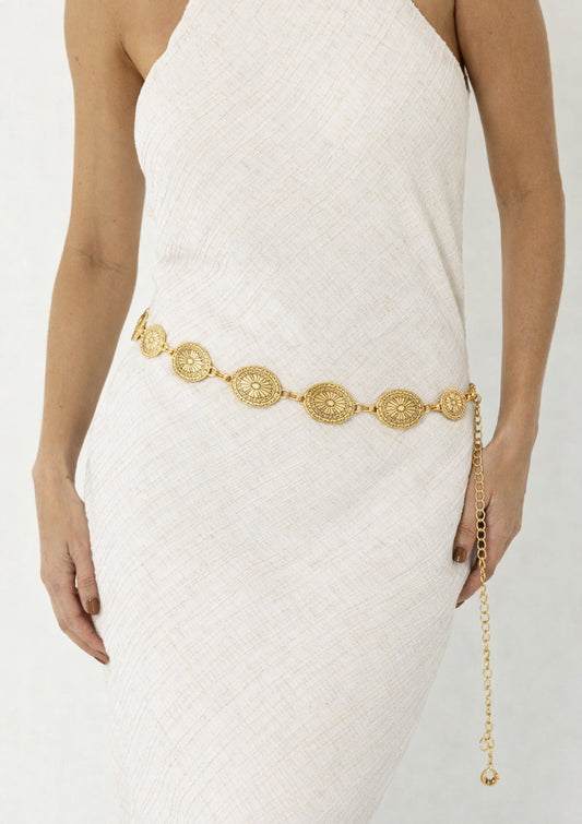 Gold belt with intricate design worn by a person in a white dress on a plain background