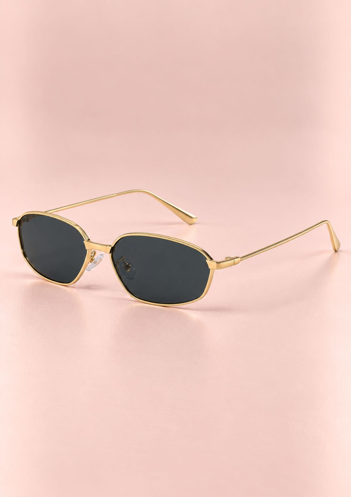 Gold-framed sunglasses with dark tinted lenses, displayed on a soft pink background.