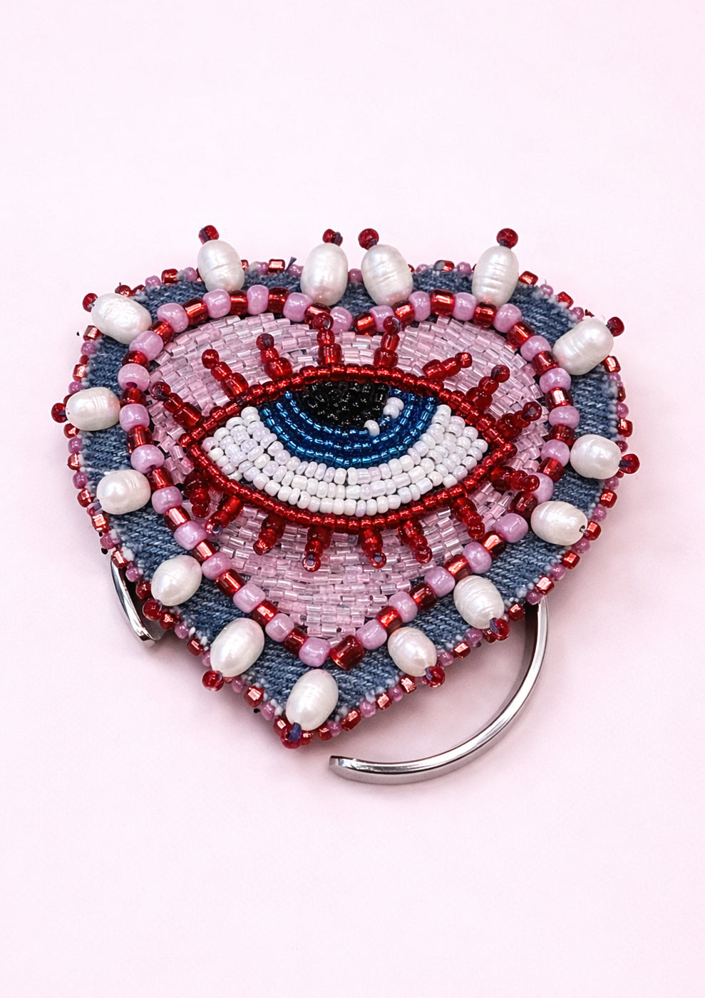 Heart-shaped beaded accessory with eye design on a pink background