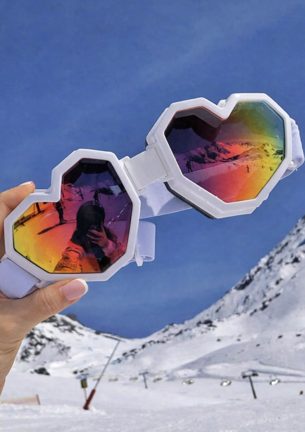 Heart-shaped sunglasses with colorful lenses held up against a snowy mountain background