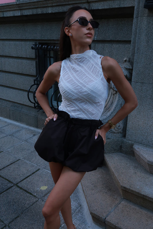 Woman in a white sleeveless top and black shorts standing on steps.
