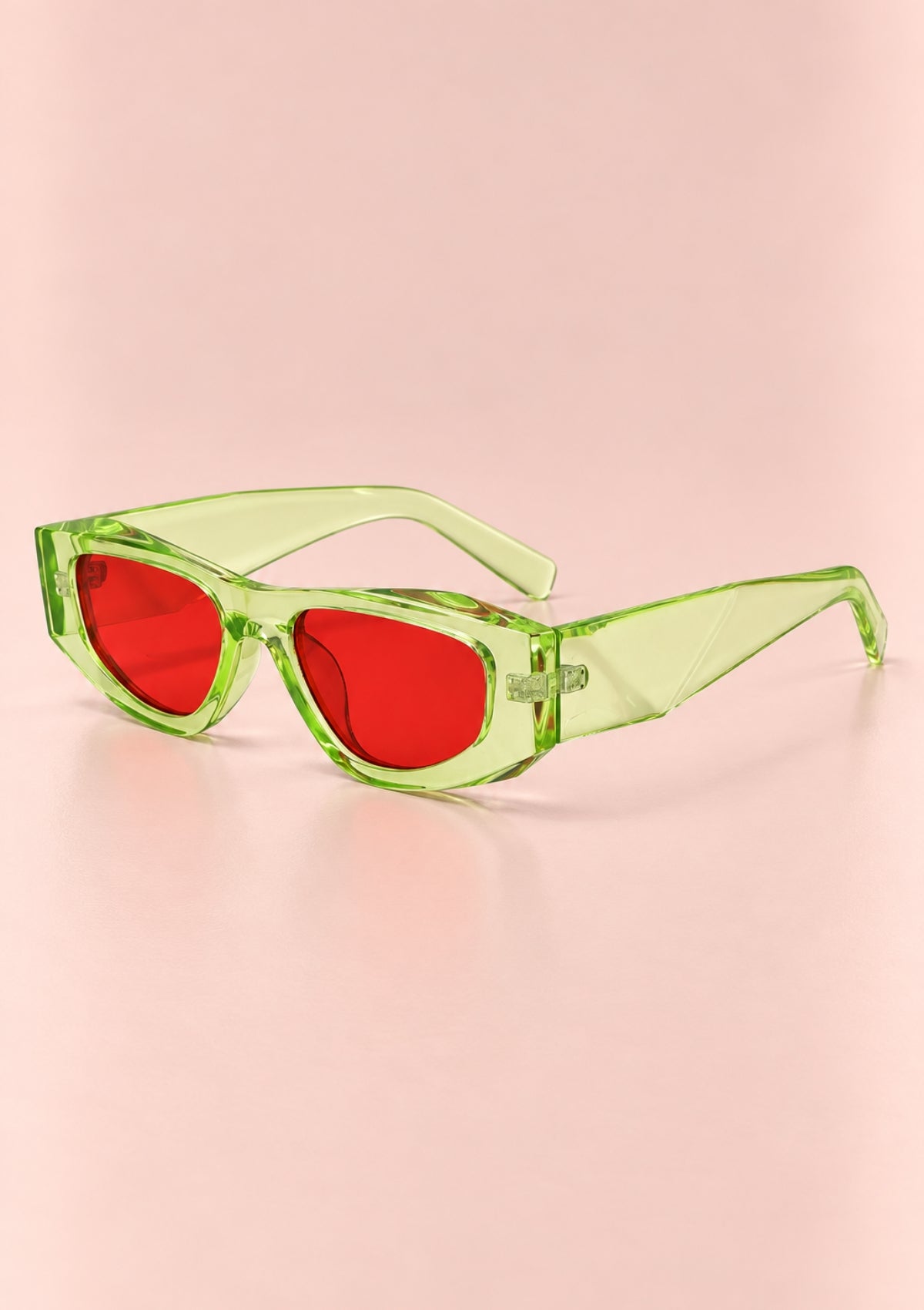 Green translucent sunglasses with red lenses, shown on a soft pink background.