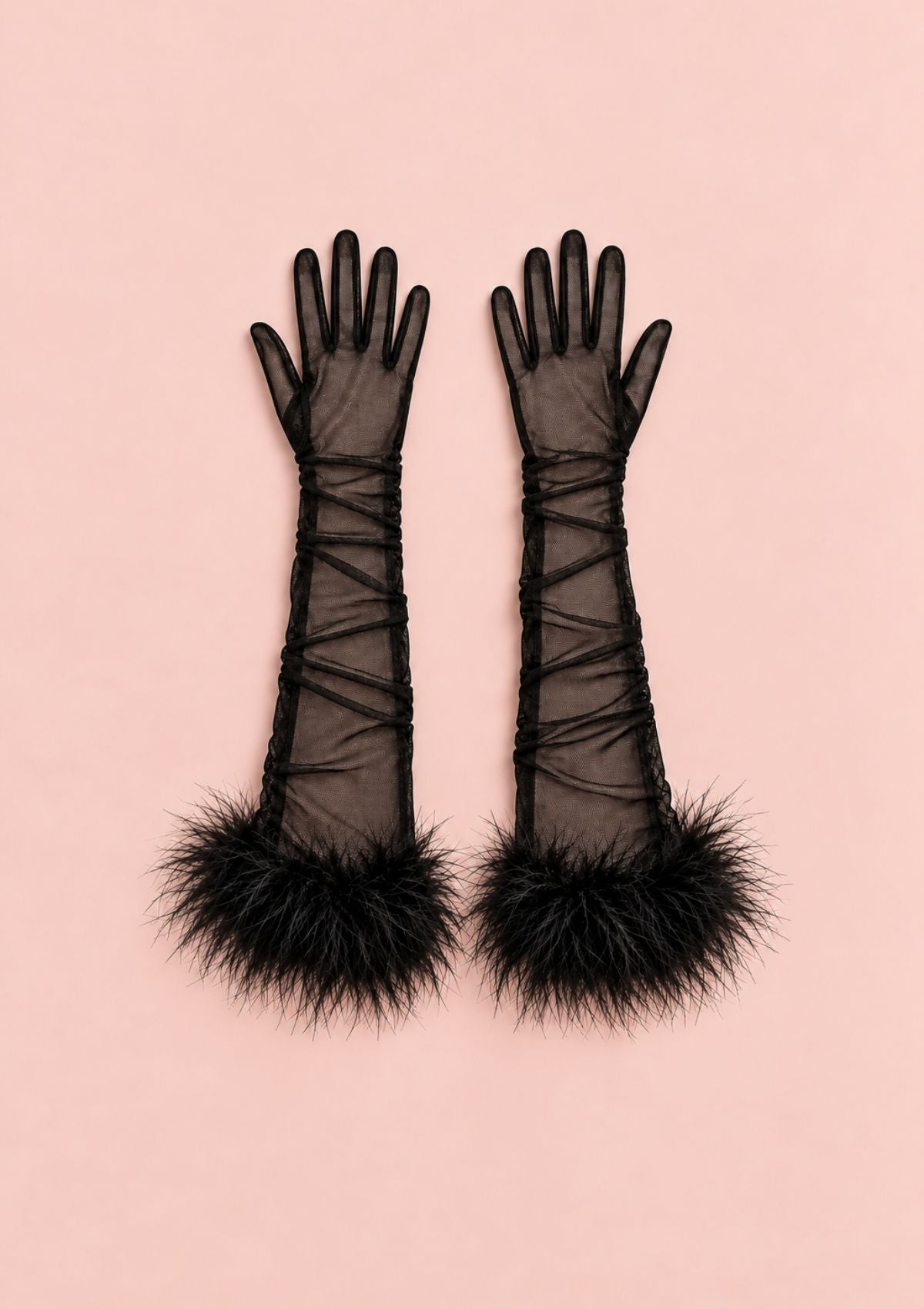 A pair of long black sheer gloves with lace-up cuffs and fluffy black feather trim at the wrists, laid flat on a solid light pink background.