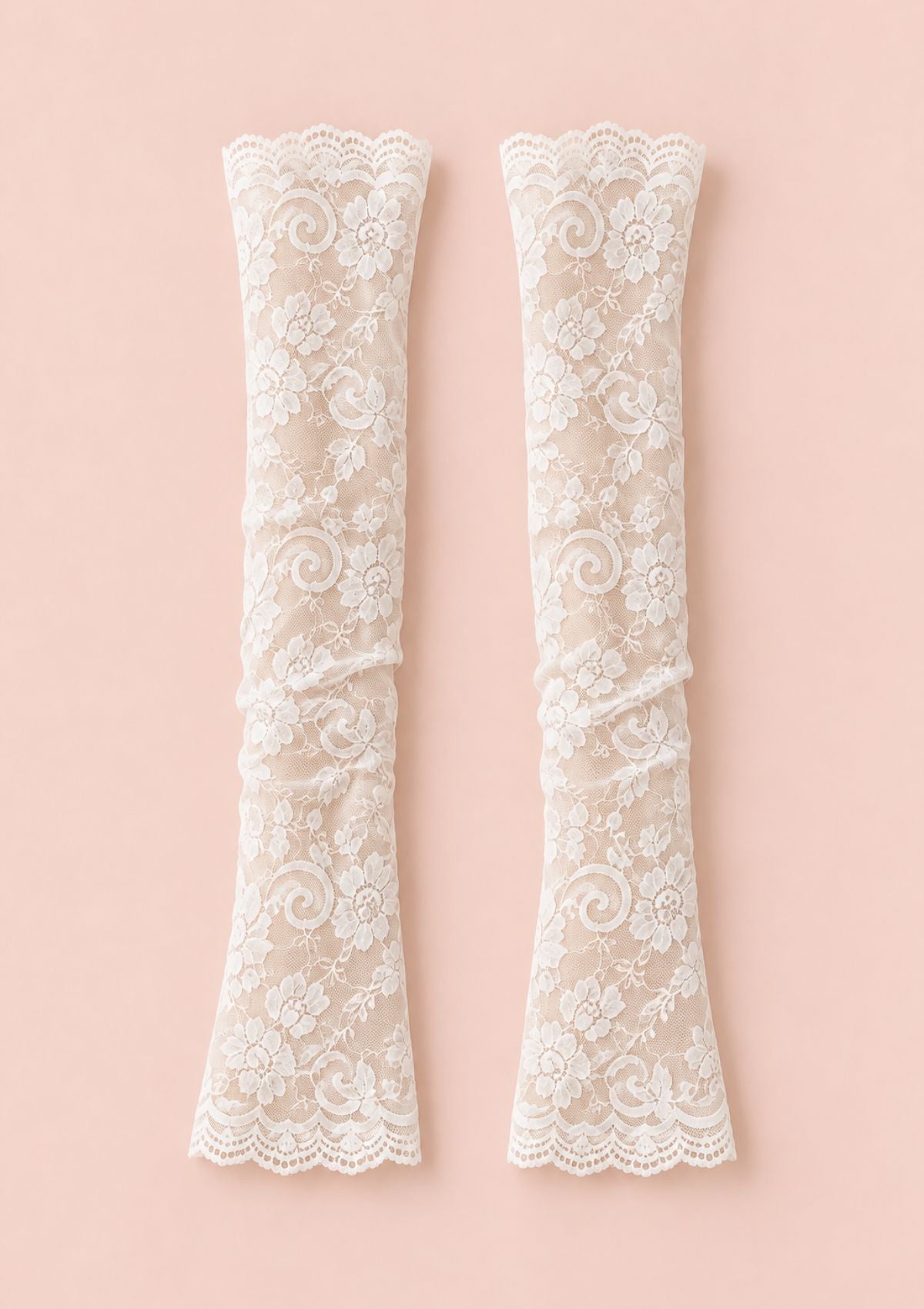 A pair of long cream lace gloves with floral patterns and scalloped edges, displayed flat against a solid pale pink background.