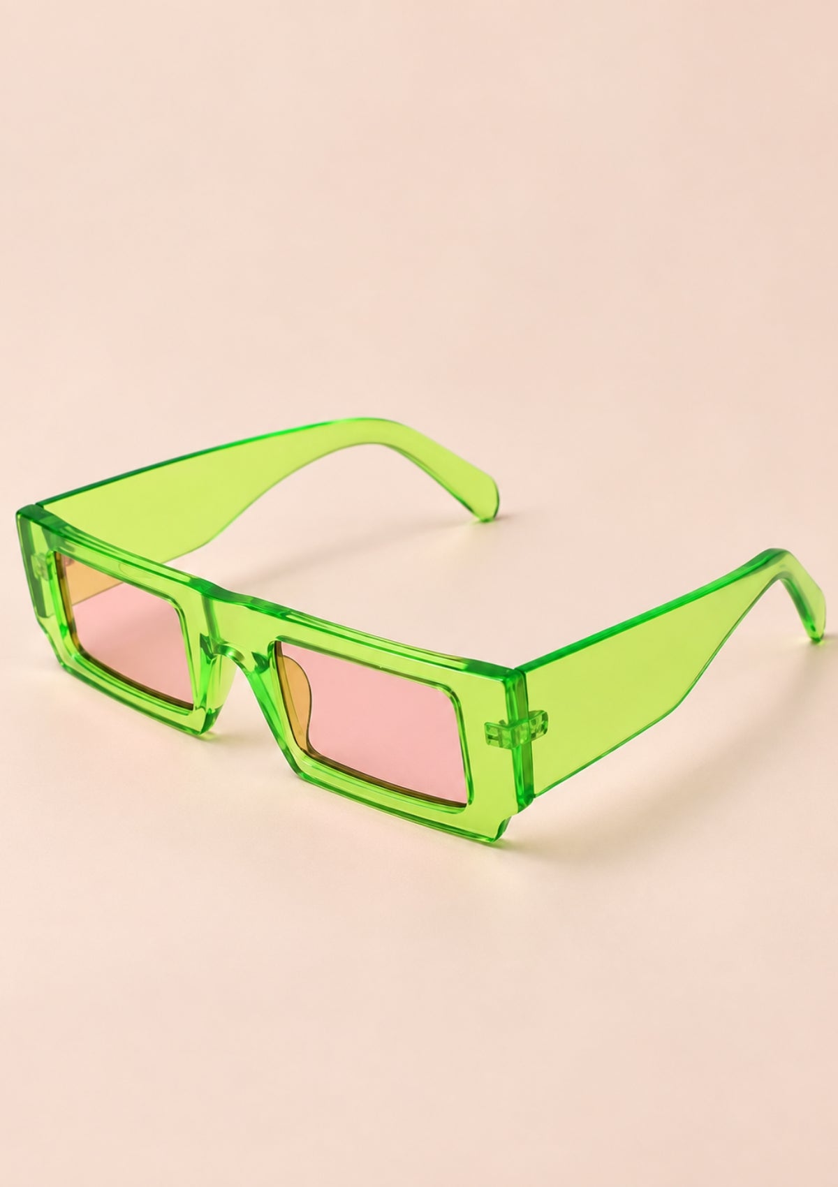 Green translucent square sunglasses with pink tinted lenses, displayed on a solid pale peach background.