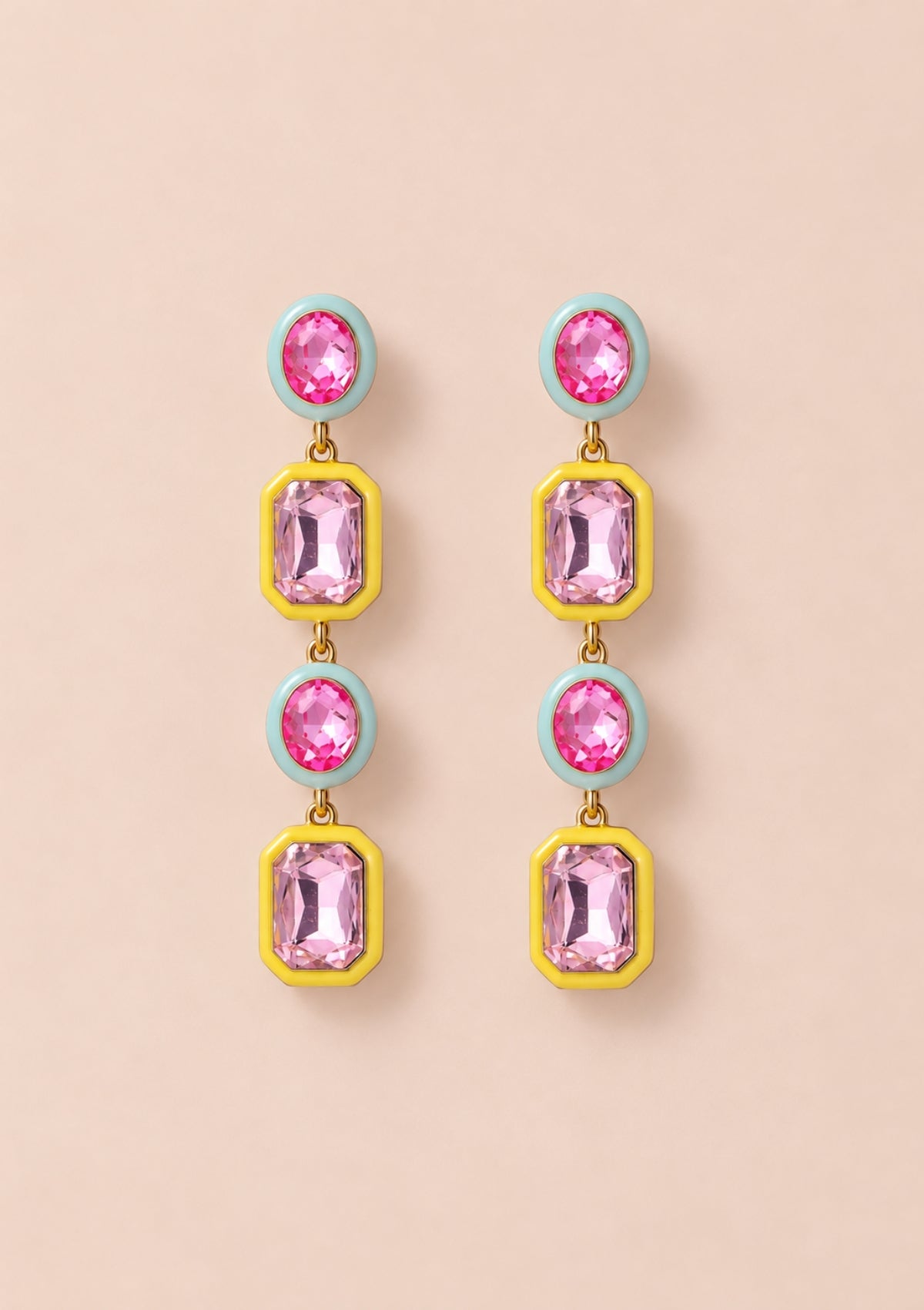 A pair of drop earrings with pink gemstones in yellow and mint green settings, displayed on a solid pale peach background.
