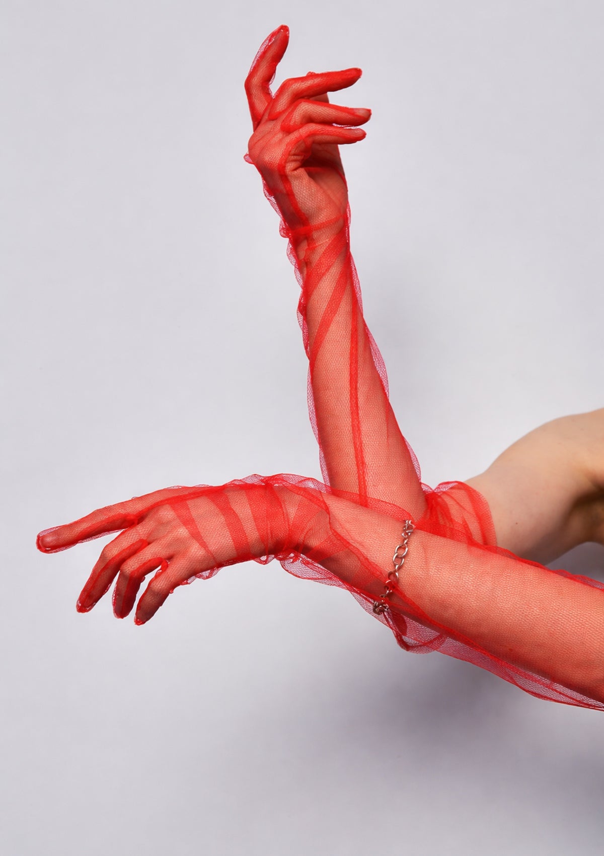 Red fishnet gloves worn by a person on a light gray background