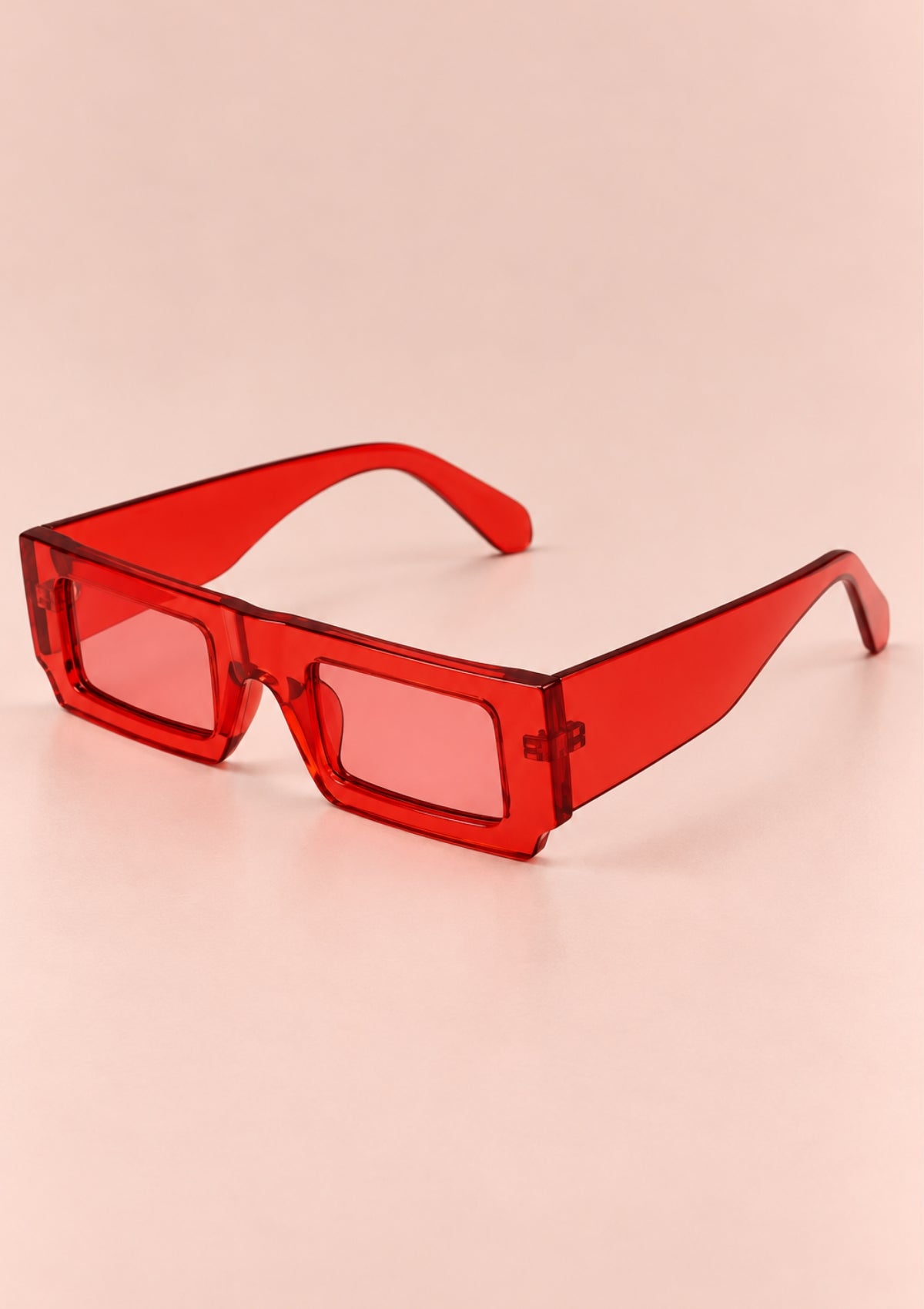Red translucent square sunglasses with thick frames and pink-tinted lenses, photographed on a soft peach-pink background.