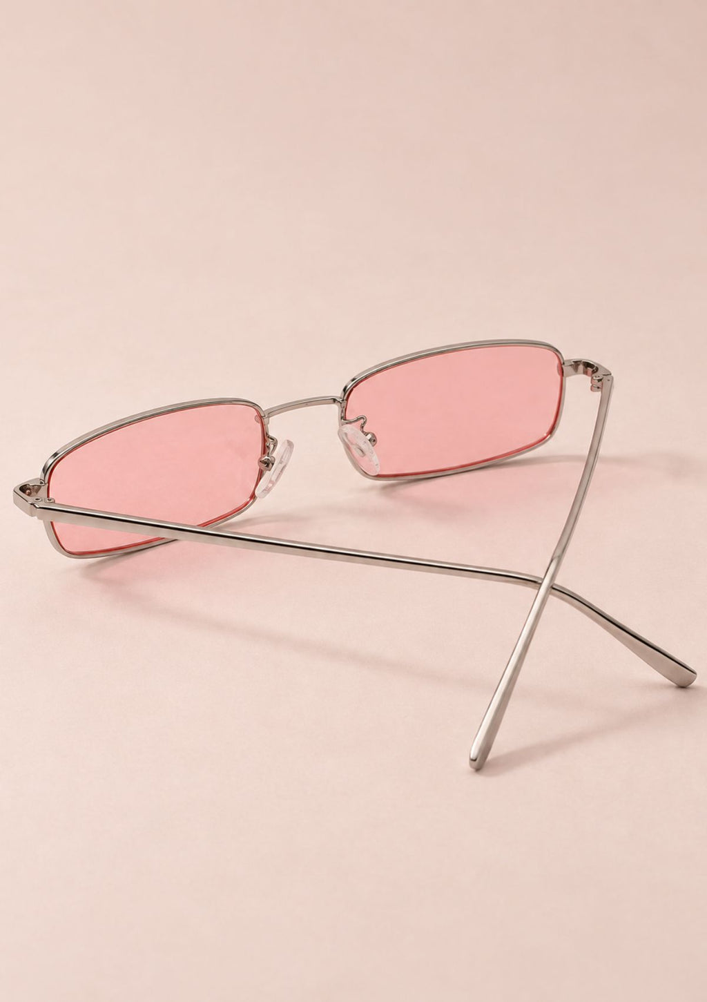 Rectangular metal-framed sunglasses with pink tinted lenses, displayed on a soft pink background.