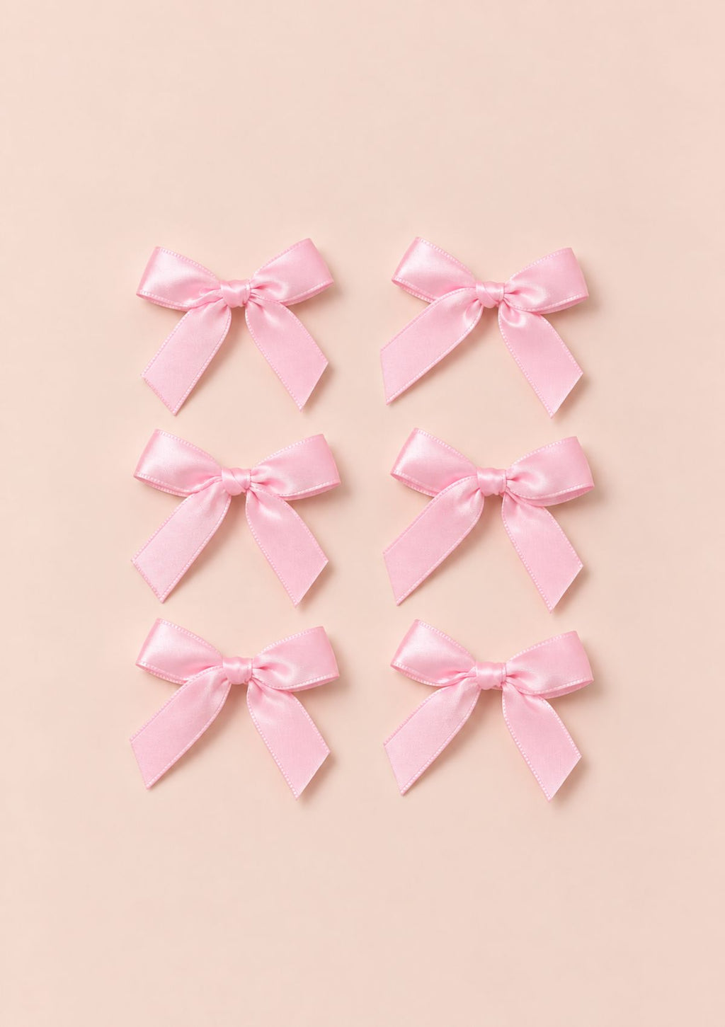 Set of six pink satin bows arranged on a pale blush background.