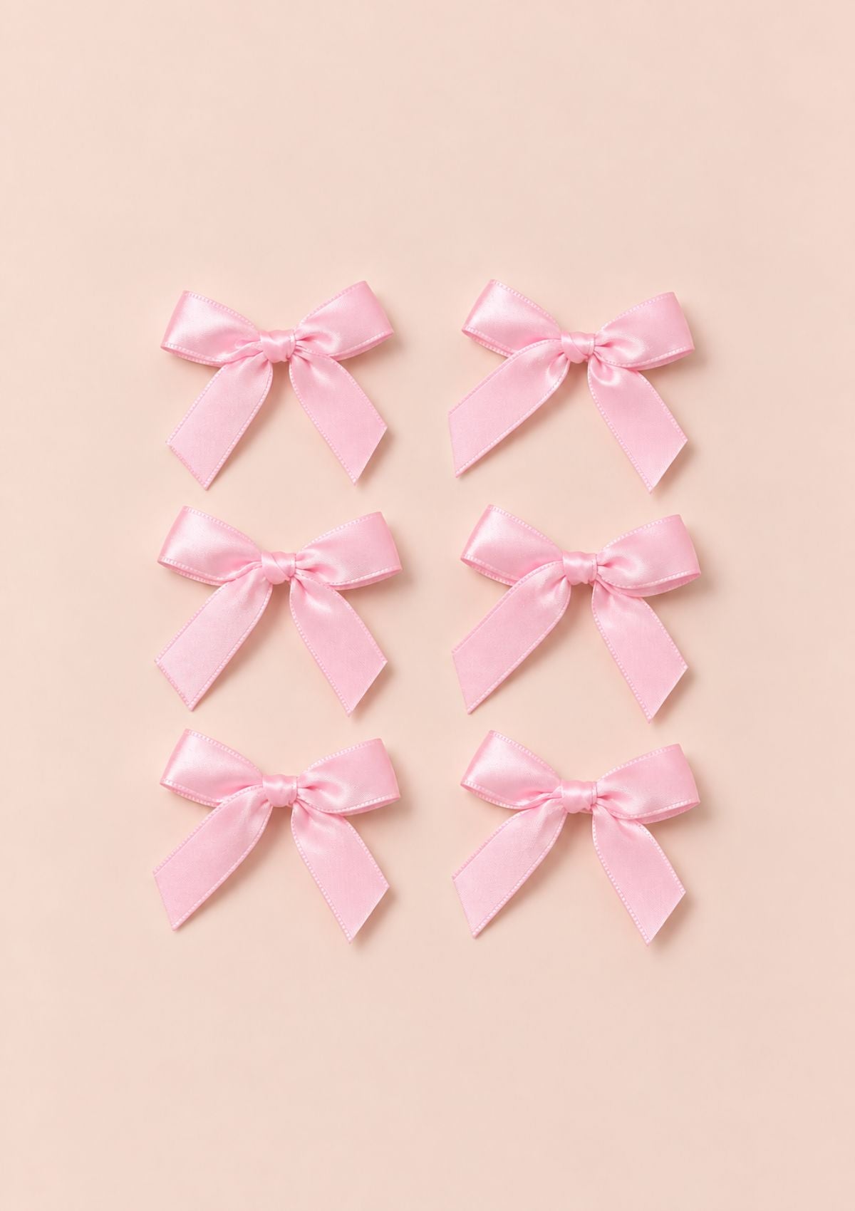 Set of six pink satin bows arranged on a pale blush background.