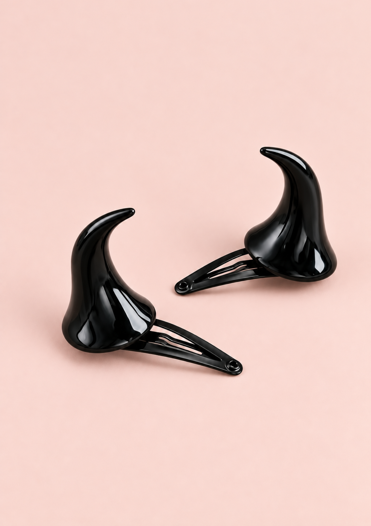 Set of two glossy black horn-shaped hair clips with clip fastenings displayed on a pale pink background.