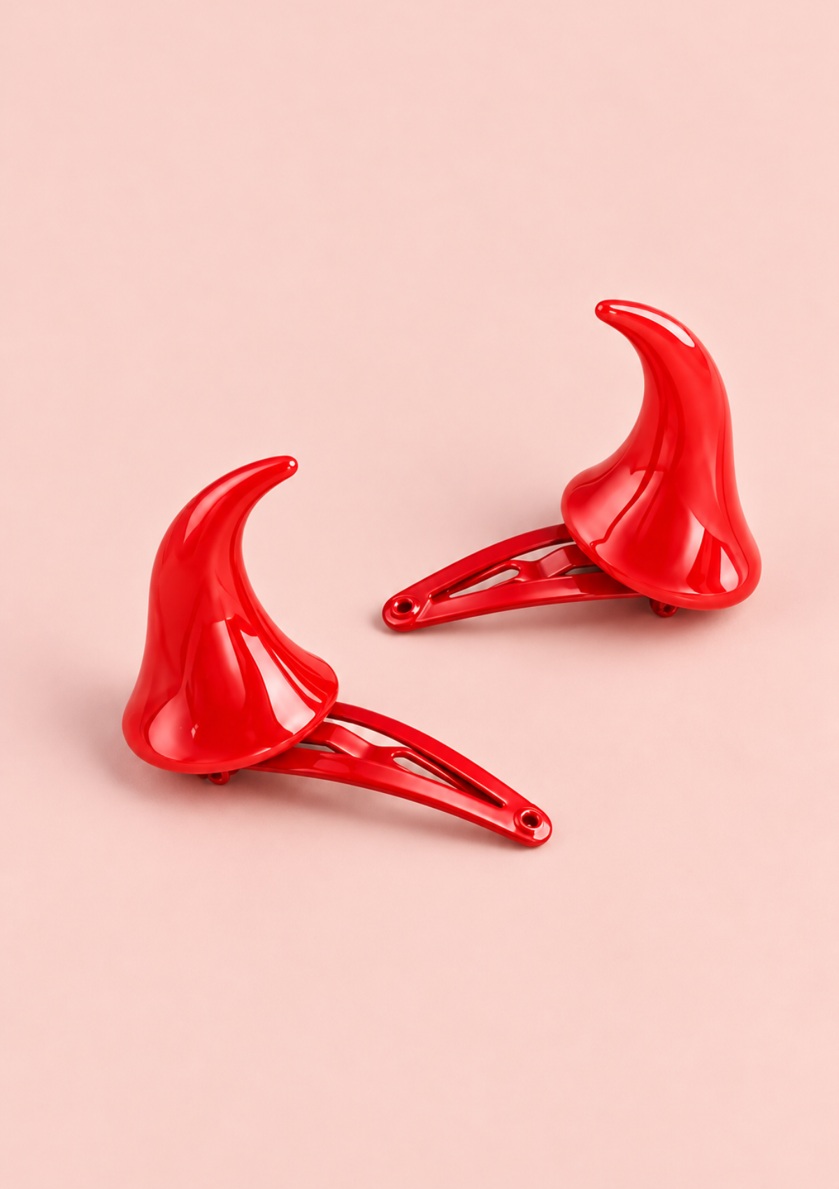 Set of two glossy red horn-shaped hair clips displayed on a pale pink background.