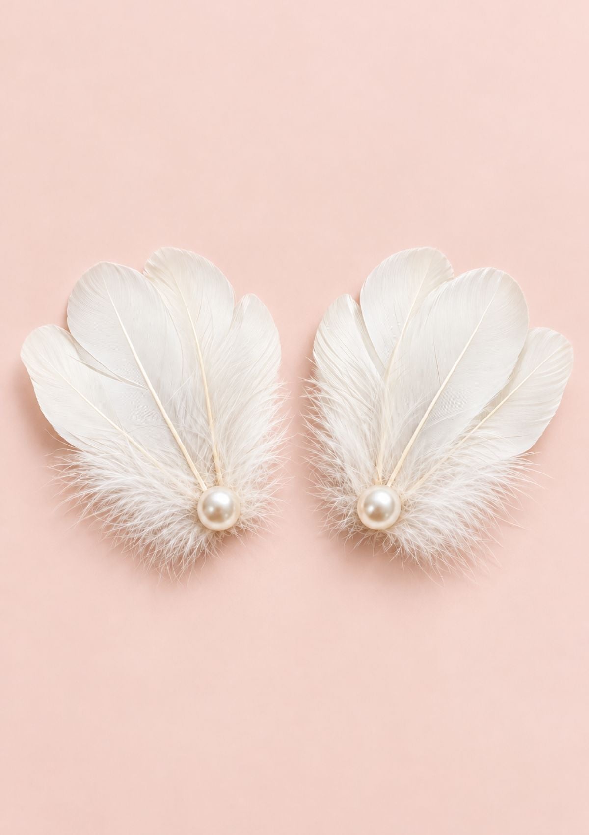A pair of white feather drop earrings with a small pearl at the center, displayed on a soft pink background.