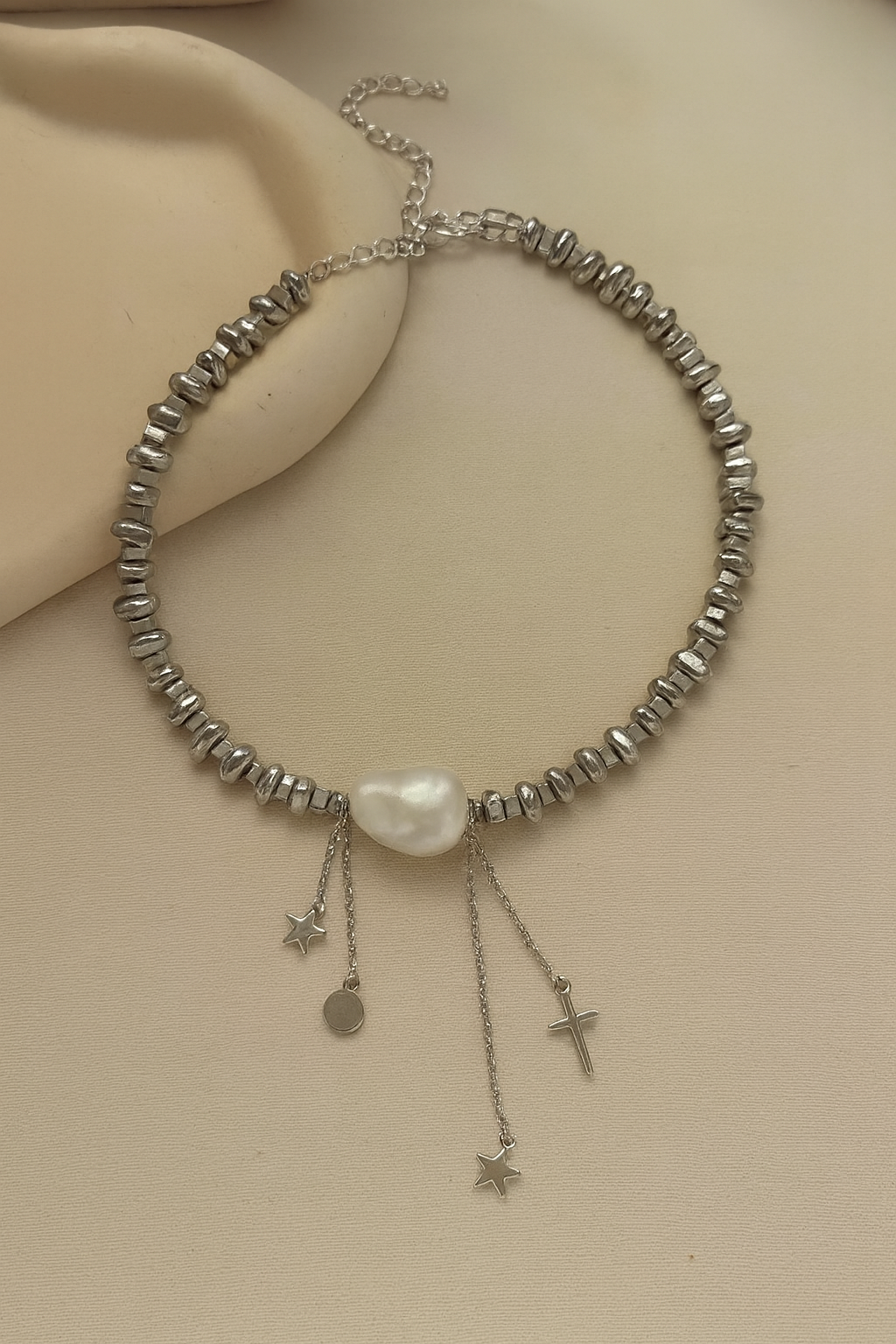 Silver beaded necklace with a pearl and charms on a beige surface