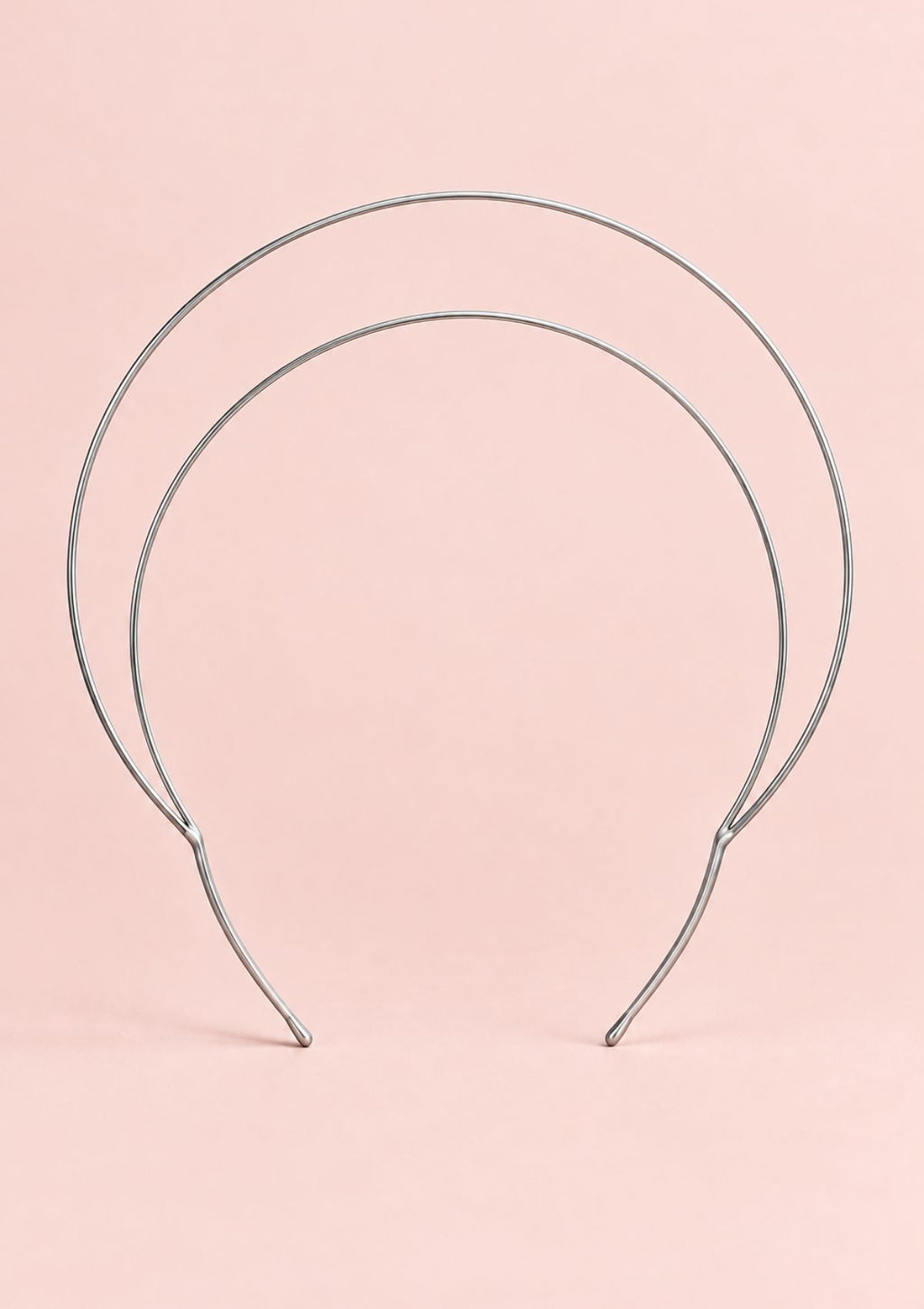 Silver halo crown headband with a minimalist double-loop metal design on a pale pink background.